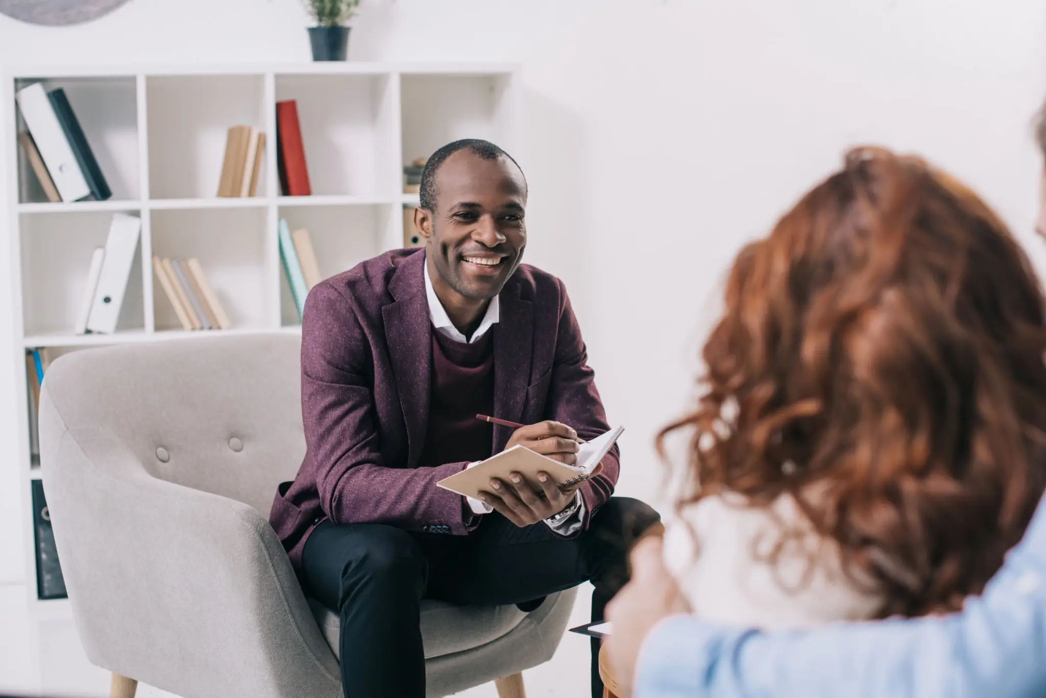 Man in purple sweater talking to a woman in a therapy session.