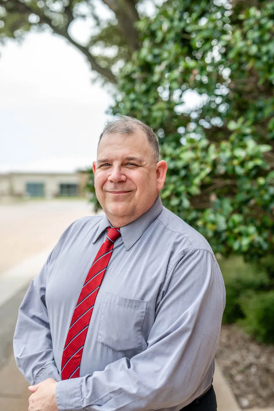 Smiling man in a gray shirt and red tie outdoors.